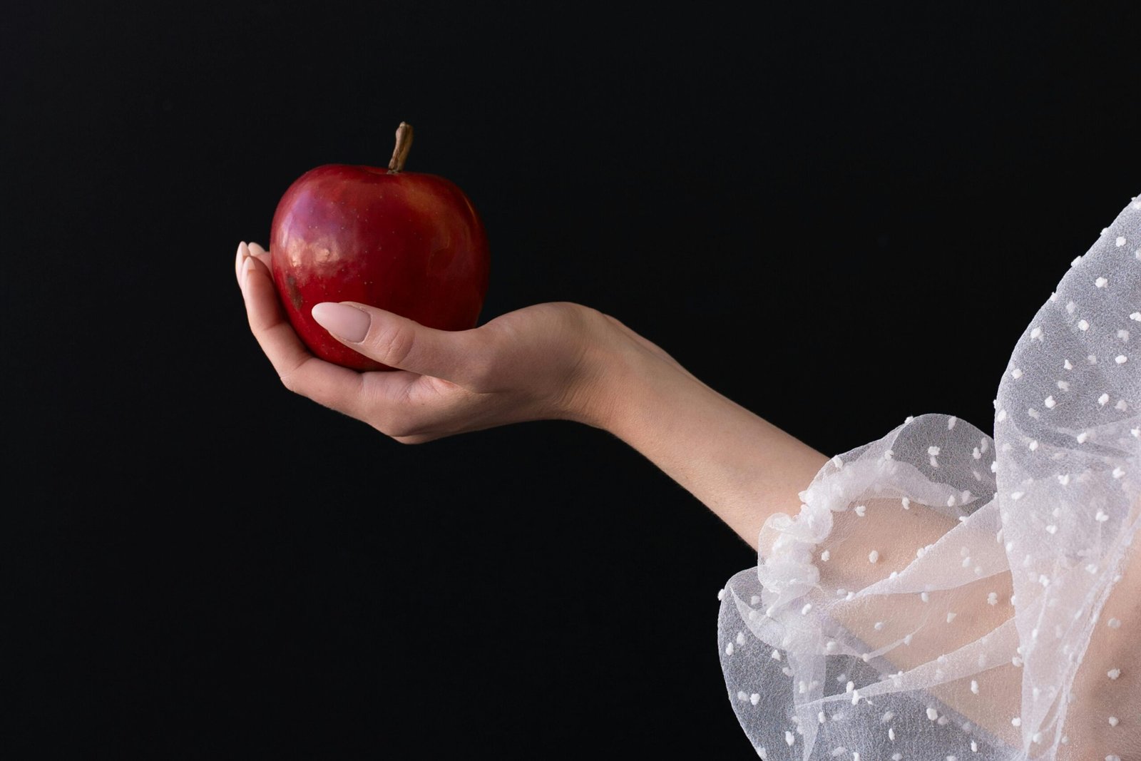A graceful hand holds a red apple against a dark backdrop, symbolizing temptation and beauty.